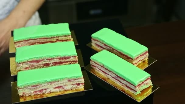 Confiseur en uniforme de chef met des portions de gâteau multicouche crémeux glacé vert — Video