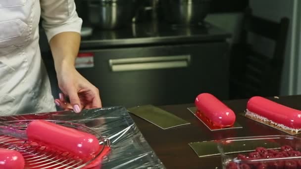 Кондитер в белой форме кладет розовый овальный десерт на золотой стенд — стоковое видео