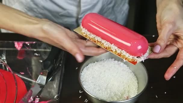 Женские руки, украшающие розовый овальный десерт из мусса с кокосовой стружкой — стоковое видео