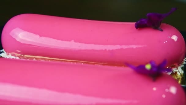 Gros plan panorama vers le bas à rose glacé desserts ovales avec décoration de fleurs violettes — Video