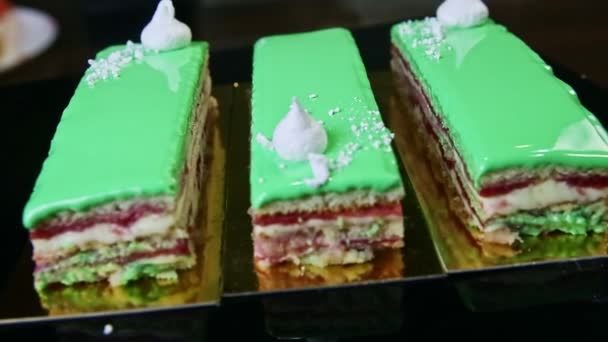 Zwart spiegelblad met drie groen geglazuurde laagjes cake porties draait rond — Stockvideo