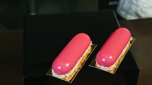 Draufsicht auf zwei rosa glasierte Desserts mit Kokosraspeln auf schwarzem Spiegeltablett — Stockvideo