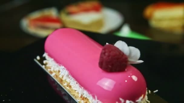 Dessert ovale glacé rose simple avec fleur et framboise tourne sur support noir — Video