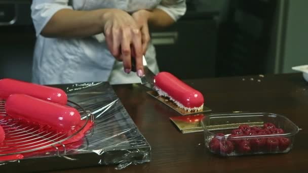 Confectioner by hands with knife puts pink glazed oval cake on golden stand — Stock Video