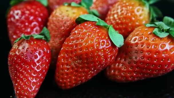 Macro view en grupo de fresas rojas jugosas frescas maduras enteras servidas en negro — Vídeos de Stock