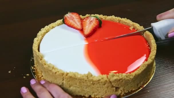 Confeiteiro por mãos cortes na metade por faca cheesecake vitrificado com morangos fatiados — Vídeo de Stock