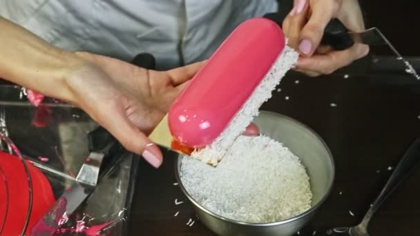코코넛 조각을 사용하여 분홍색 유약을 입힌 무스 타원 디저트를 장식하고 있는 과자 — 비디오