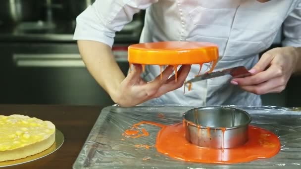 Confectioner removes excess of orange glaze from round cheesecake by knife — Stock Video