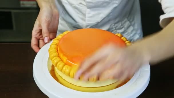 Frau in weißer Uniform dekoriert orange glasierten Käsekuchen mit Mini-Makronen — Stockvideo