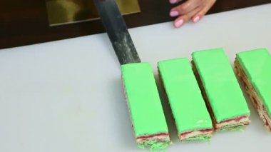 Şekerlemecinin en üst görüntüsü, yeşil katmanlı kekin bir porsiyonunu altın tezgahın üzerine koyar.