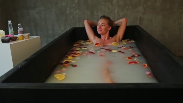 Junges schönes blondes Mädchen badet mit Milch, Rosenblättern und Zitrusscheiben — Stockvideo