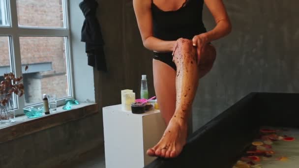 Крупный план блондинка стройная девушка в черном нижнем белье делает кожу ног пилинг кофе скраб — стоковое видео