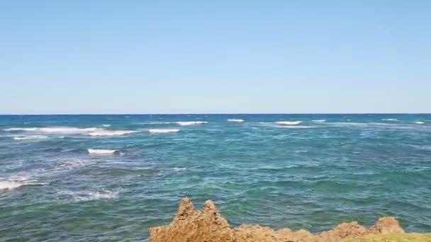 Langsames Panorama auf weiße Wellen im blauen Ozean, die sich an der felsigen Küste auflösen — Stockvideo