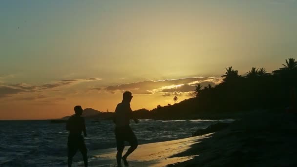 Black silhouettes of two strong men running on ocean shore against sunset sky — Stock Video