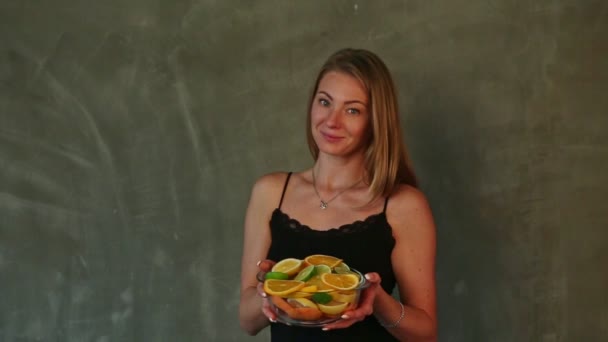 Close-up jong mooi blond meisje houdt diepe transparante kom met citrusvruchten plakjes — Stockvideo