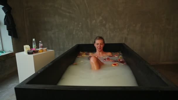 Beautiful young slim blond girl taking bath with milk, rose petals and citrus slices — Stock Video