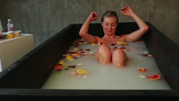 Mladá hezká dívka relaxující v černé vaně s mlékem, okvětními lístky růží a citrusovými plátky — Stock video