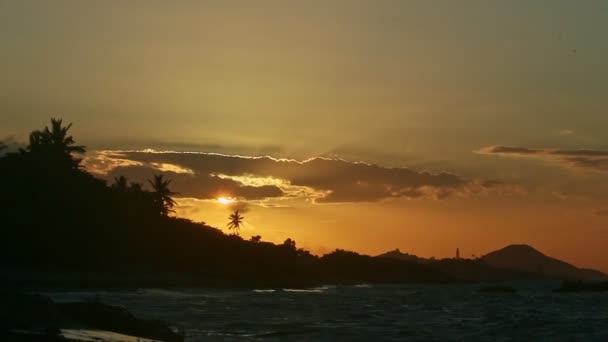 Zoom avant au soleil jaune se couchant derrière de grands nuages et des silhouettes de palmiers — Video