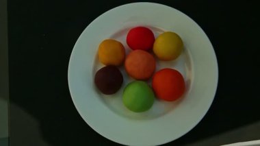 Üst kattaki kadın eli, renkli badem ezmesi parçalı beyaz tabağı alır.