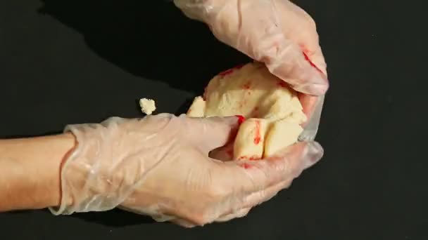 Вид зверху на людські руки замішують великий шматок білого марципана з червоним барвником — стокове відео