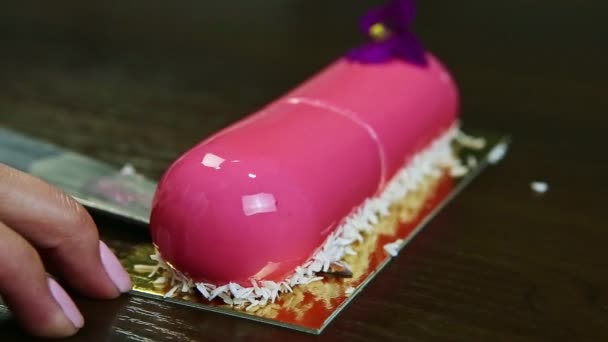 Confectioner takes away by knife one half of pink glazed oval cake with violet flower — Stock Video