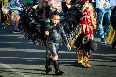Siyah Malefiz kostümlü küçük bir kız Dominik karnavalında şehir caddesinde yürüyor.