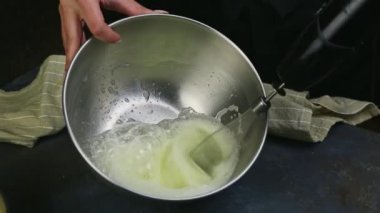 Yakın plan kadın elleri derin metal kasede çırparak yumurta akı çırpıyor.