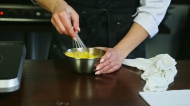 Yakın plan kadın elleri çırpın çırpın çırpın çiğ yumurta sarılarını metal kasede şekerle karıştırın