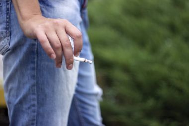 Yeşil arka plan üzerinde elinde bir sigara tutan kız. Zararı 