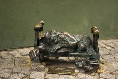 Wroclaw, Polonya - 31 Ekim 2019. Minyatür heykel, sokakta bir yatakta uyuyan cüce. Eski Wroclaw şehrinin merkezinde bulunan bronz cüce, yeşil duvar arka planı.