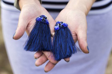 Genç bir kadın elinde taşlı mavi kumaş küpeler tutuyor.