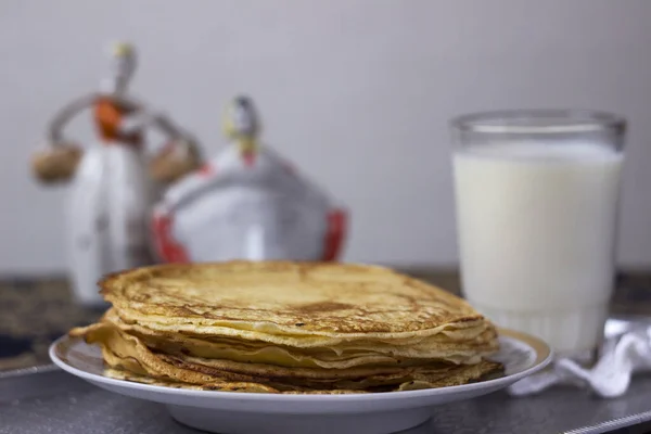 Traditional flat pancakes on a buttercup with milk, vintage ceramic figurines in the background. Slavic traditions, Shrovetide