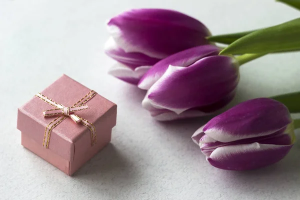 Three pink tulips with a white border on the petals lie on the table with a small pink gift box, background. Holiday concept