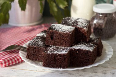 Beyaz tabakta çikolatalı kek ve kırmızı beyaz kareli peçete. Tatlı, Süt ve Çikolata Damlaları