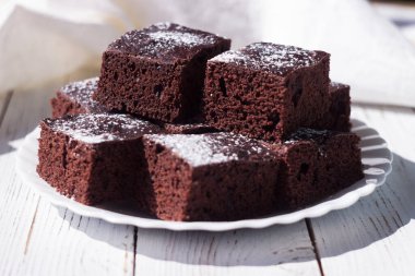 Kare parça kesilmiş çikolatalı pasta, üzerine krema serpiştirilmiş şeker, beyaz arka plan.