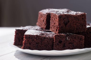 Kare parça kesilmiş çikolatalı pasta, üzerine krema serpiştirilmiş şeker, beyaz arka plan.