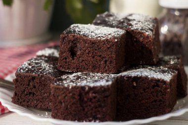 Beyaz tabakta çikolatalı kek ve kırmızı beyaz kareli peçete. Tatlı, Süt ve Çikolata Damlaları