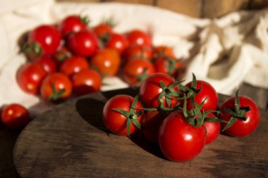 Beyaz peçeteli küçük yuvarlak domatesler, ahşap arka plan. Lezzetli sağlıklı sebzeler, çiğ yiyecekler.