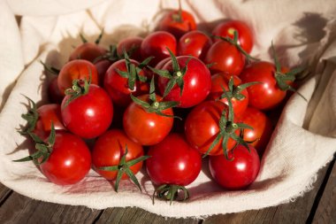 Beyaz peçeteli küçük yuvarlak domatesler, ahşap arka plan. Lezzetli sağlıklı sebzeler, çiğ yiyecekler.