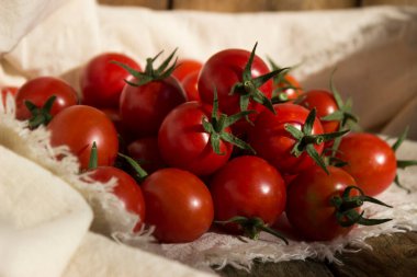 Beyaz peçeteli küçük yuvarlak domatesler, ahşap arka plan. Lezzetli sağlıklı sebzeler, çiğ yiyecekler.