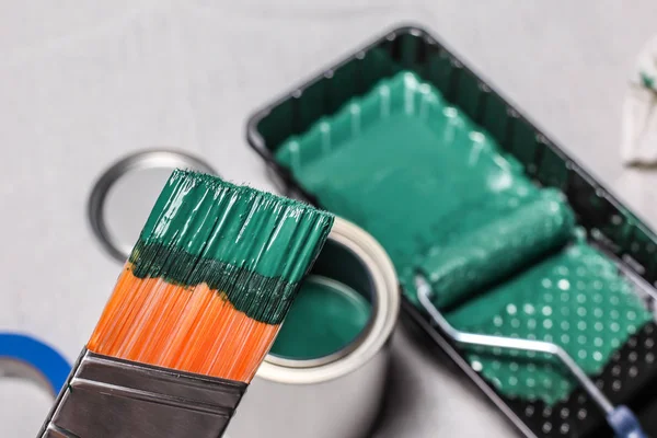 Hand with paintbrush and green paint and other tools — Stock Photo, Image