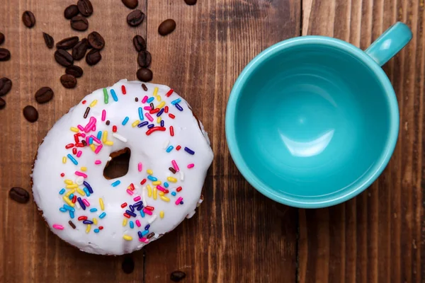 Кофейные зерна с пончиком и чашкой кофе на деревянном столике — стоковое фото