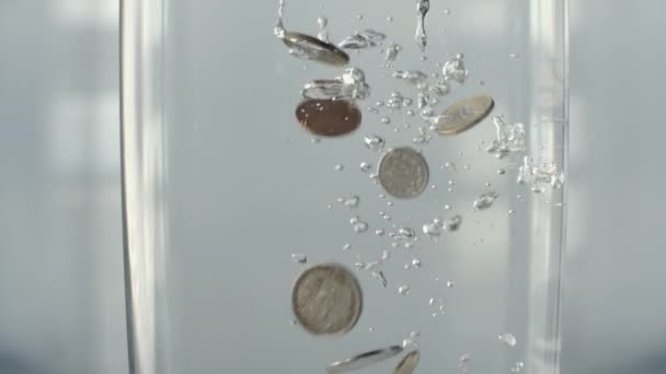Κέρματα πέφτουν στο ποτήρι του νερού νερό — Αρχείο Βίντεο