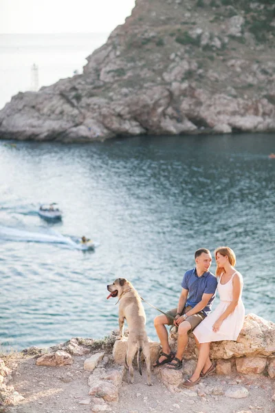 Пара парней, играющих со своей собакой на горе возле океана — стоковое фото