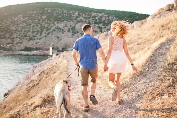 Casal de caras brincando com seu cão na montanha perto do oceano — Fotografia de Stock