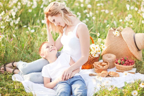 Мать устраивает пикник с сыном на цветущем поле ромашек — стоковое фото