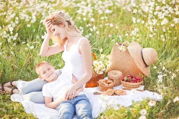 Camomi の花のフィールドに彼の息子とのピクニックを持つ母親 — ストック写真