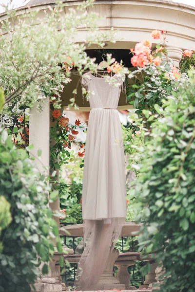 Svatební šaty visí v rotundy v kvetoucí zahradě. Svatební Ru — Stock fotografie