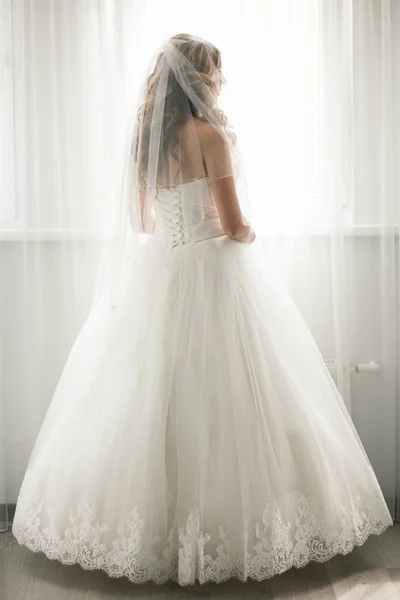 Hermosa novia en vestido de novia blanco mirando en la ventana —  Fotos de Stock