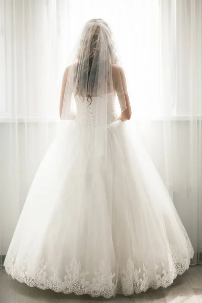 Vackra bruden i vit brudklänning titta i fönster — Stockfoto